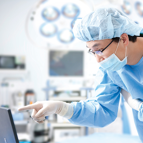 Surgeon in full surgical attire pointing at a screen in an operating room, representing the advanced medical procedures at 365MC Clinic